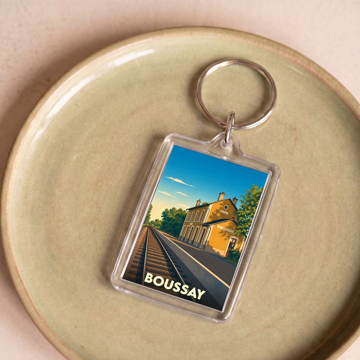 Porte-clés souvenir de la ville de Boussay avec une illustration stylisée d'une gare sous un ciel bleu.