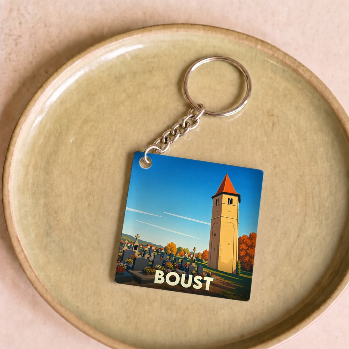 Porte-clés souvenir de la ville de Boust avec une illustration stylisée de son église et de son cimetière.