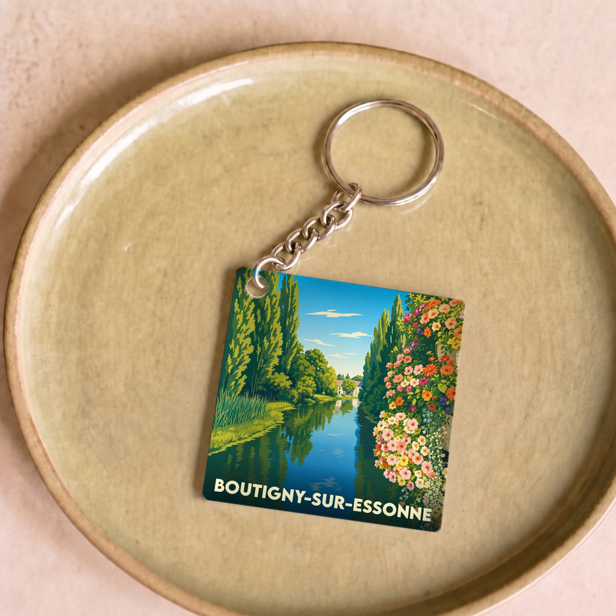 Porte-clés souvenir de la ville de Boutigny-sur-Essonne avec une illustration stylisée d'un paysage de rivière fleuri.