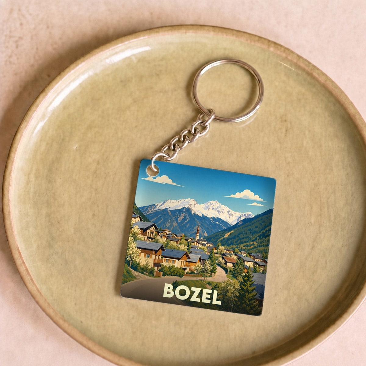Porte-clés souvenir de la ville de Bozel avec une illustration stylisée de montagnes et d'un village alpin.