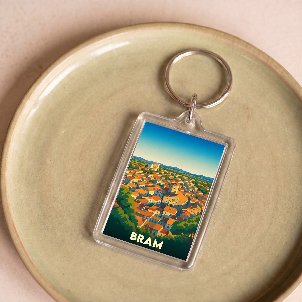 Porte-clés souvenir de la ville de Bram avec une illustration stylisée de ses toits orangés.