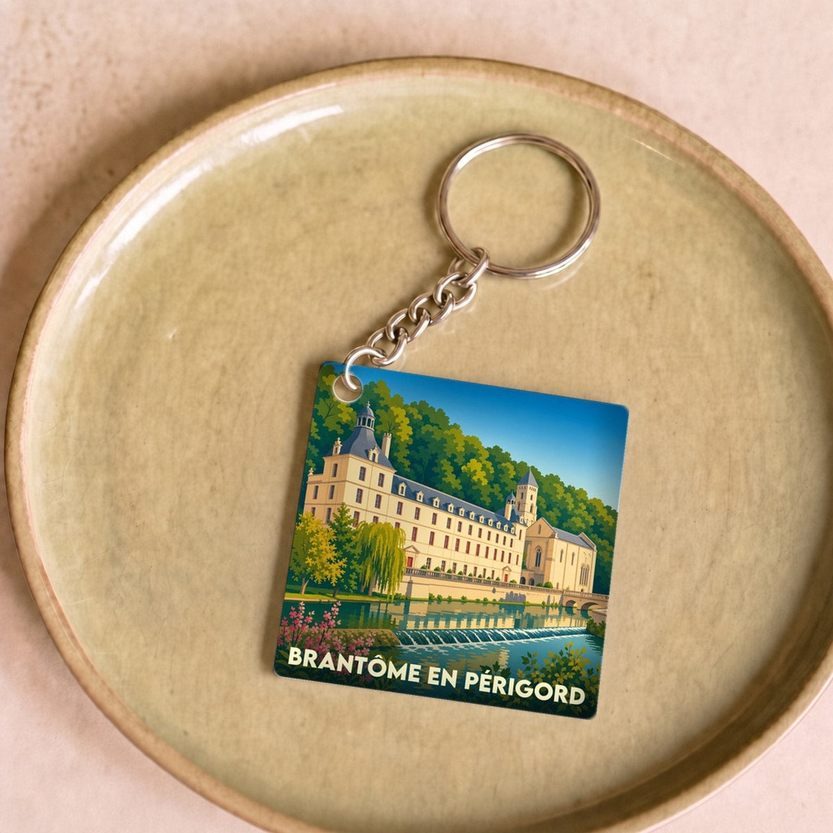 Porte-clés souvenir de la ville de Brantôme en Périgord avec une illustration stylisée de son abbaye au bord de l'eau.