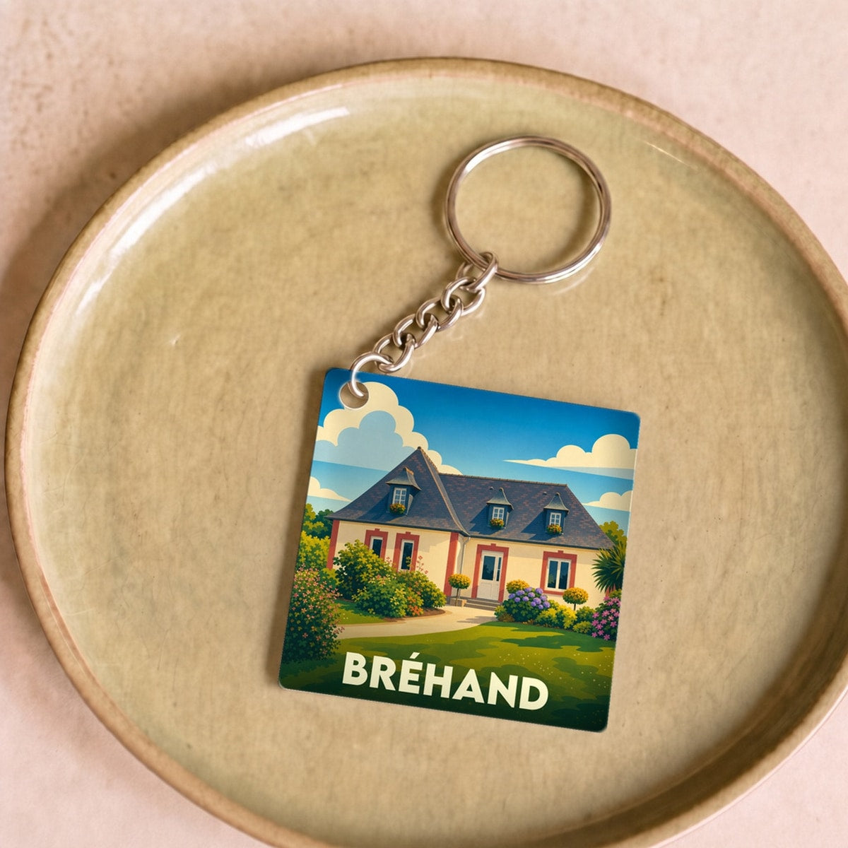 Porte-clés souvenir de la ville de Bréhand avec une illustration stylisée d'une maison régionale.