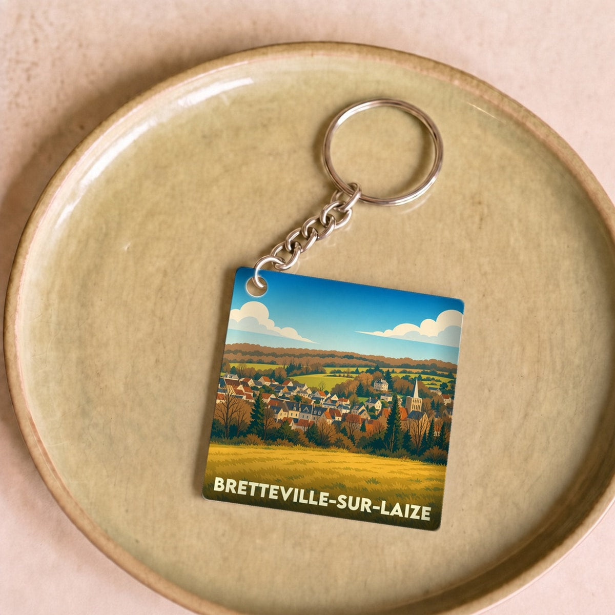 Porte-clés souvenir de Bretteville-sur-Laize avec une illustration stylisée de la ville et de ses paysages.