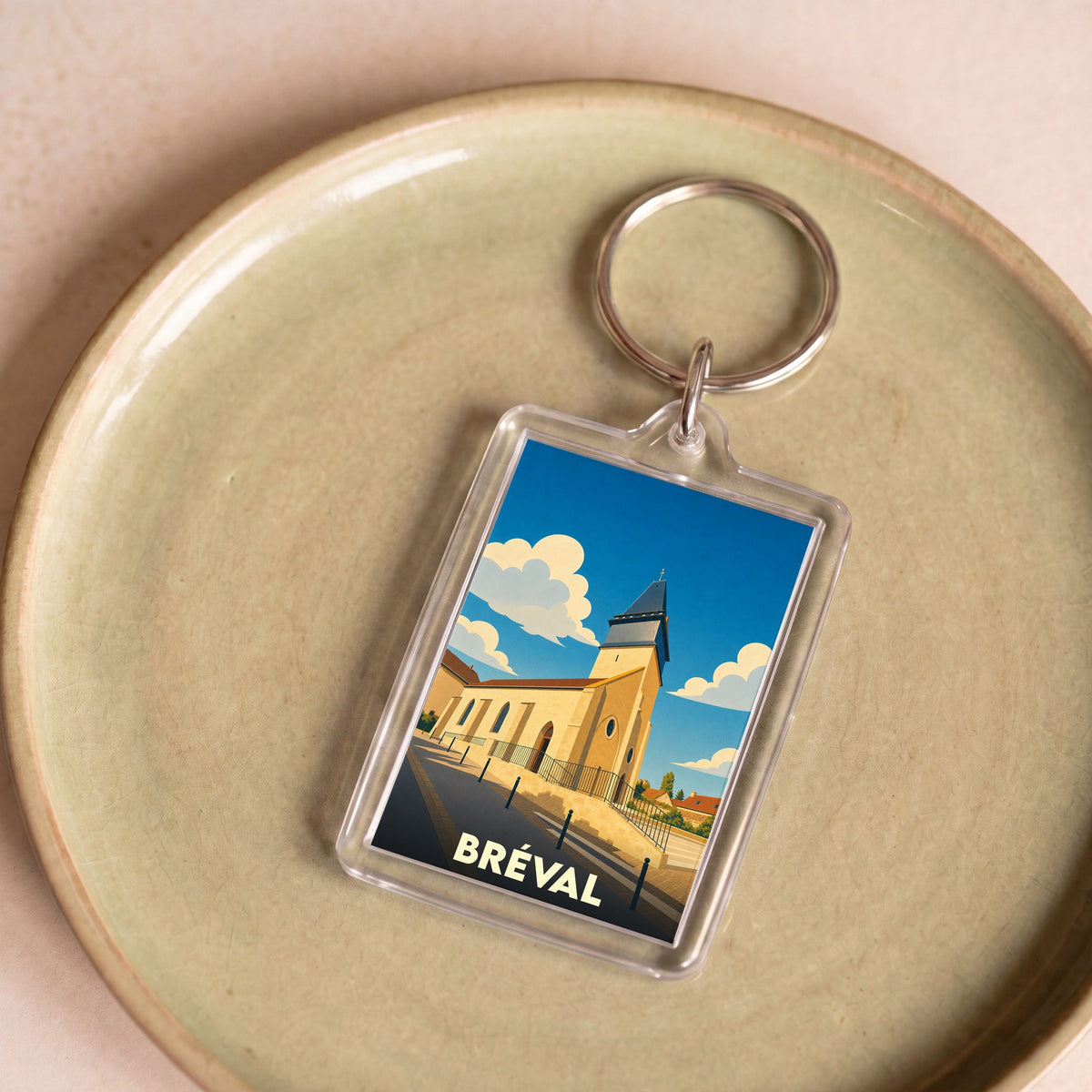 Porte-clés souvenir de la ville de Bréval avec une illustration stylisée d'une église sous un ciel bleu.