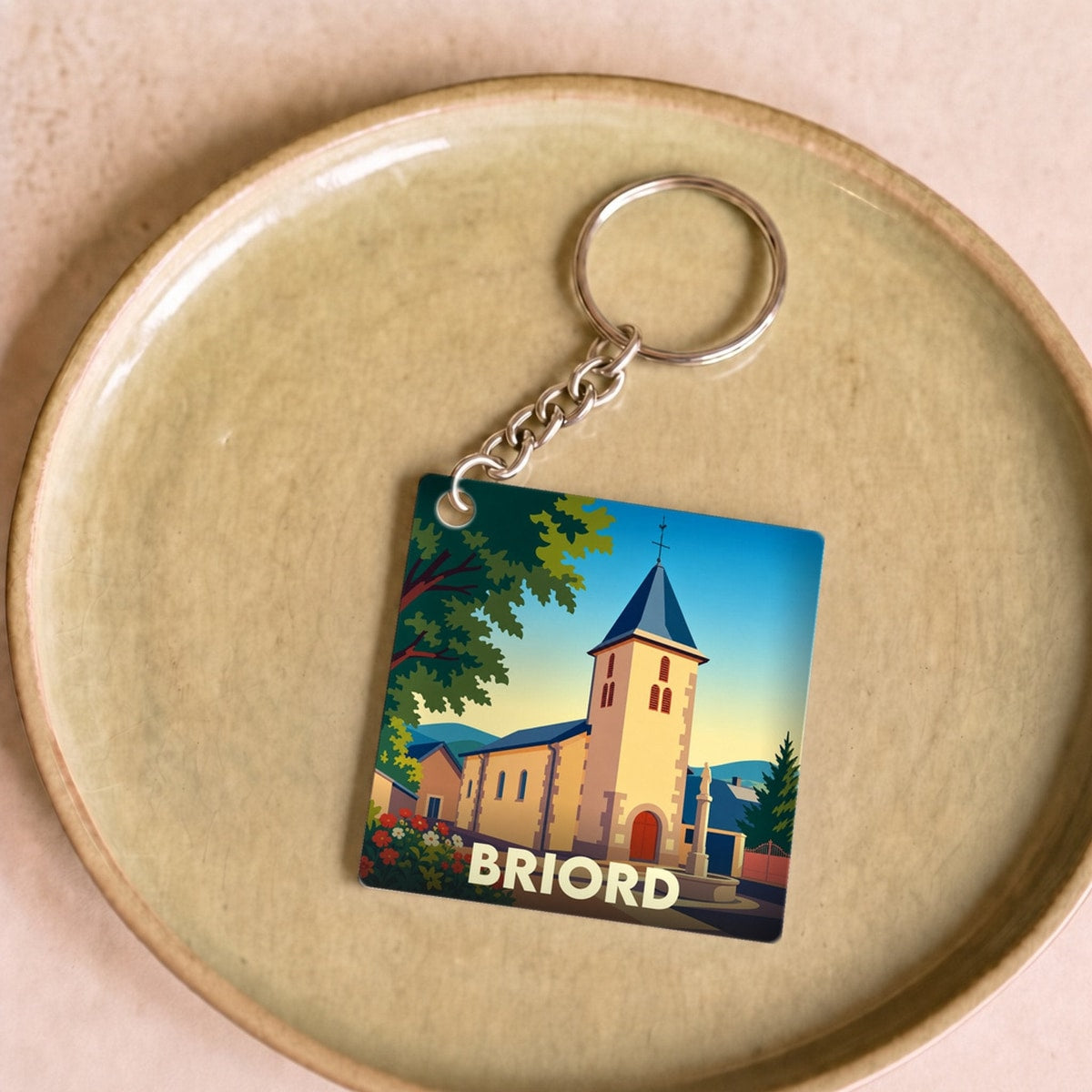 Porte-clés souvenir de la ville de Briord avec une illustration stylisée d'une église sous un ciel bleu.
