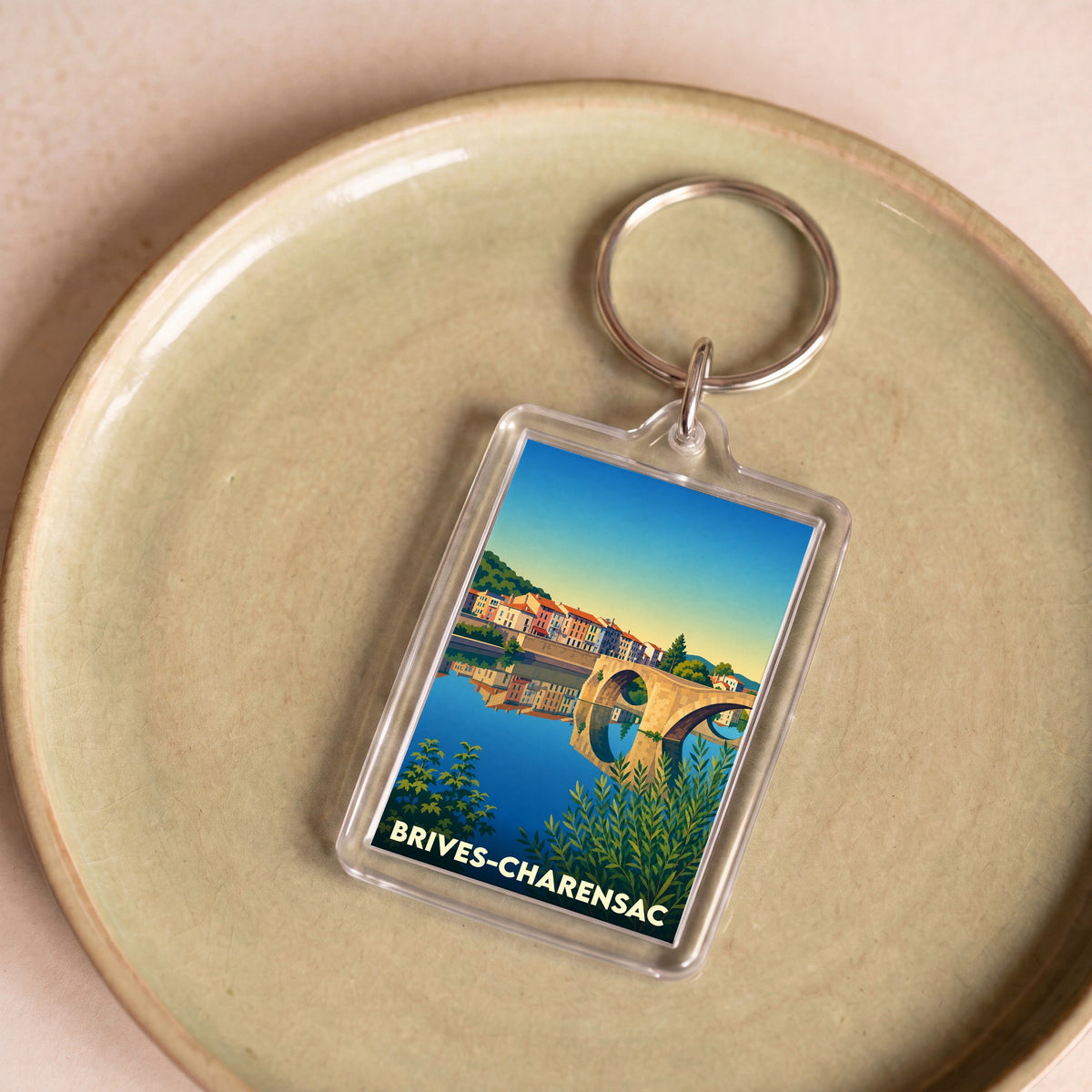 Porte-clés souvenir de la ville de Brives-Charensac illustré d'un paysage coloré avec un pont et une rivière.
