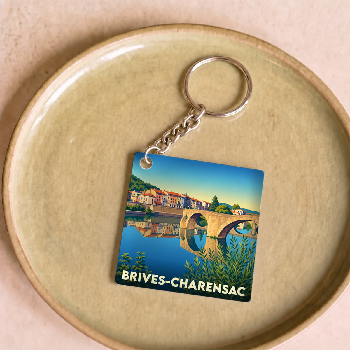 Porte-clés souvenir de la ville de Brives-Charensac illustré d'un paysage coloré avec un pont et une rivière.