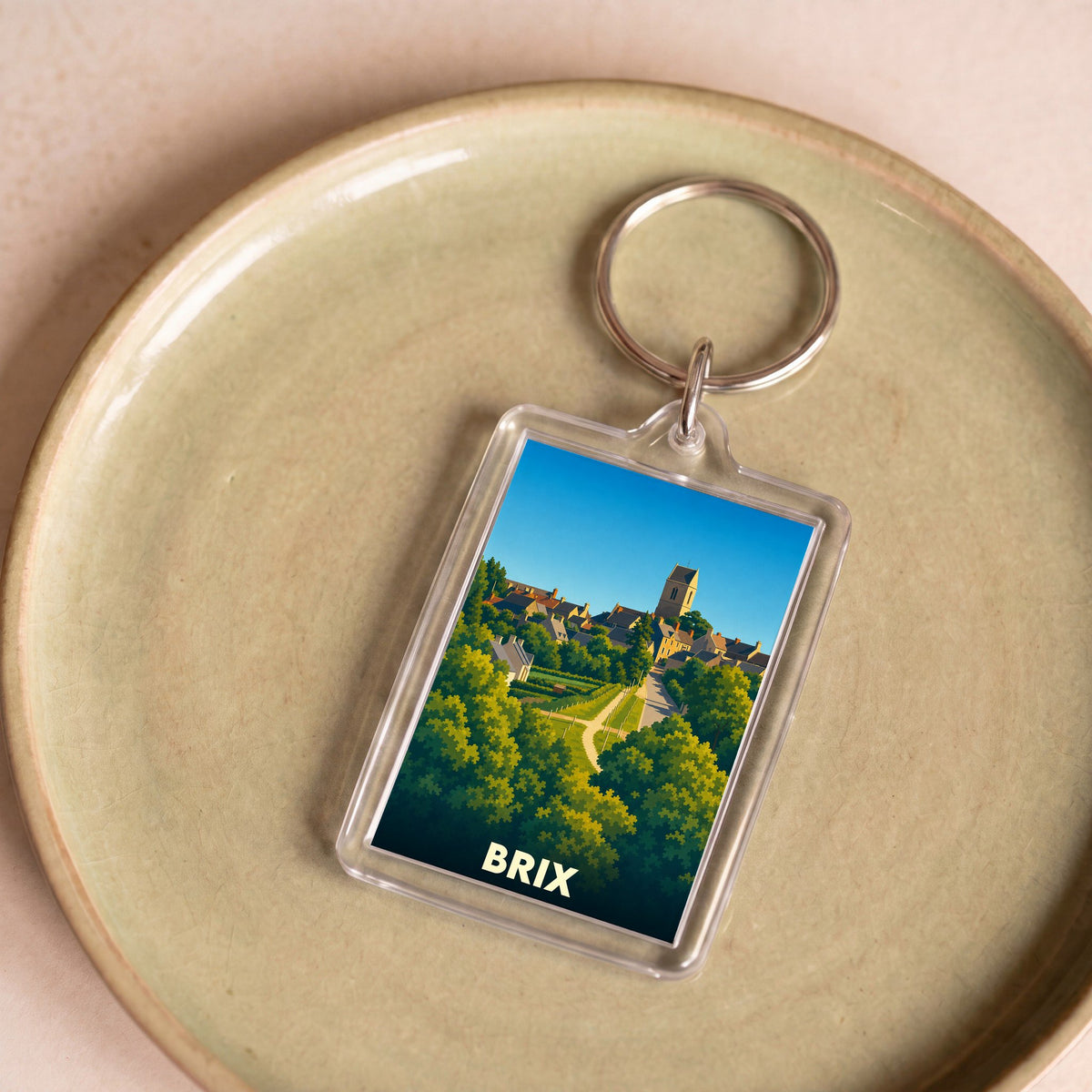 Porte-clés souvenir de la ville de Brix avec une illustration stylisée d'un paysage urbain verdoyant.