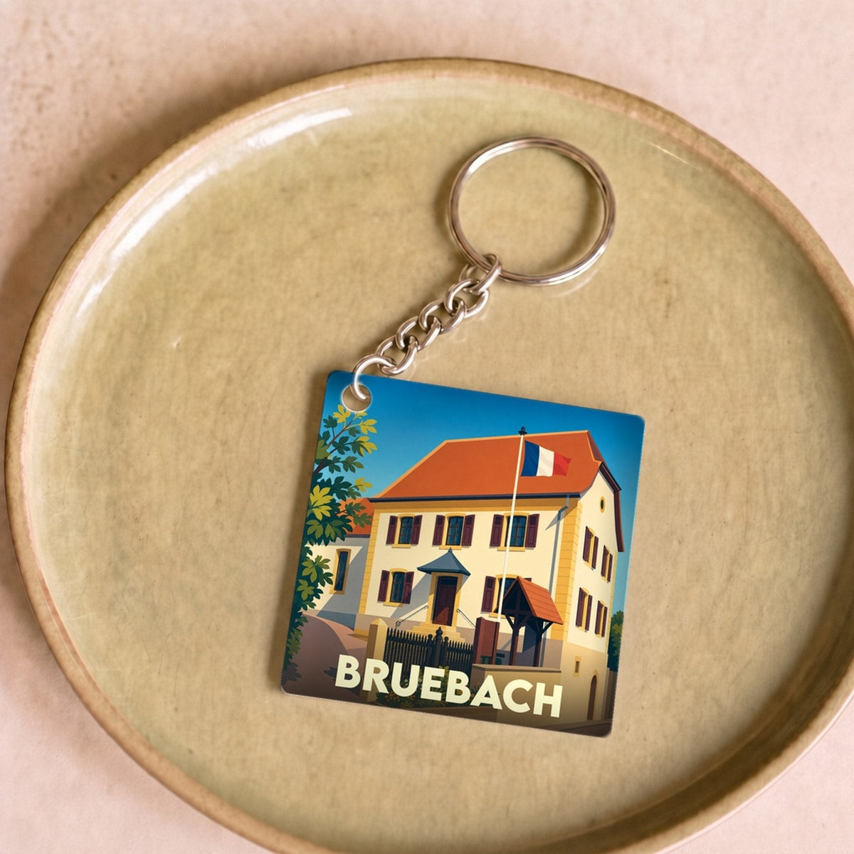 Porte-clés souvenir de la ville de Bruebach avec une illustration stylisée d'un bâtiment arborant le drapeau français.