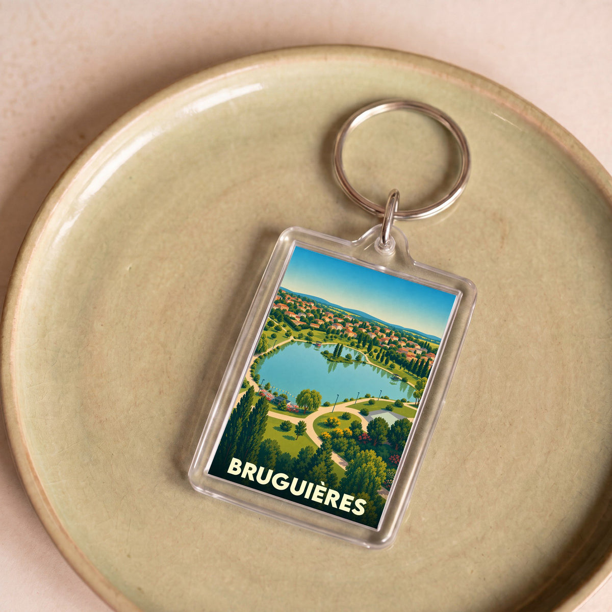 Porte-clés souvenir de la ville de Bruguières avec une illustration stylisée d'un parc et son lac.