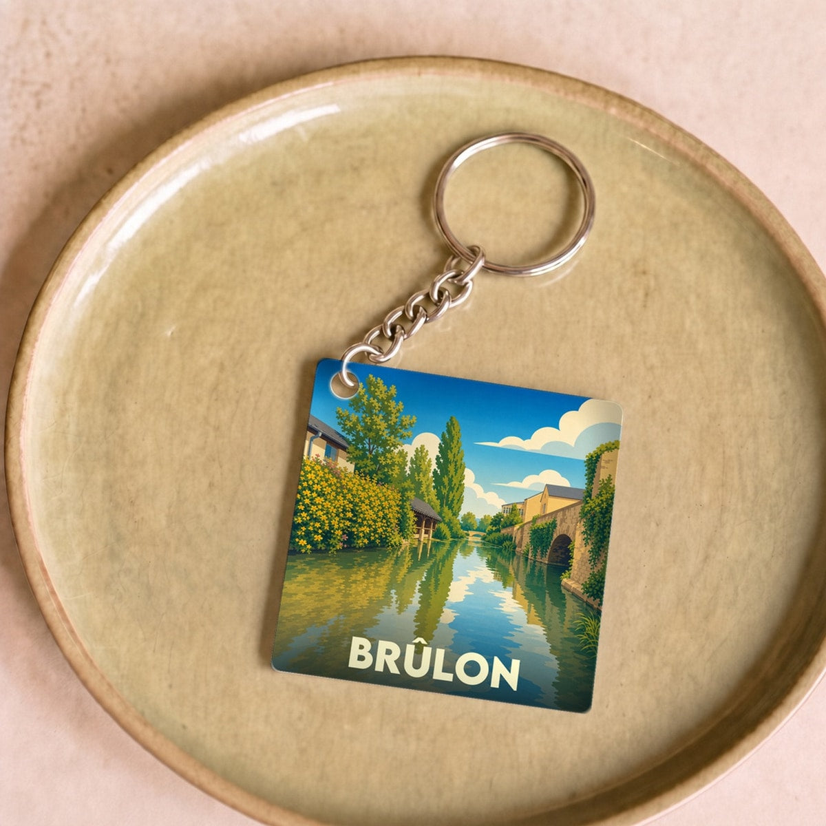 Porte-clés souvenir de la ville de Brûlon avec une illustration stylisée d'un paysage fluvial.