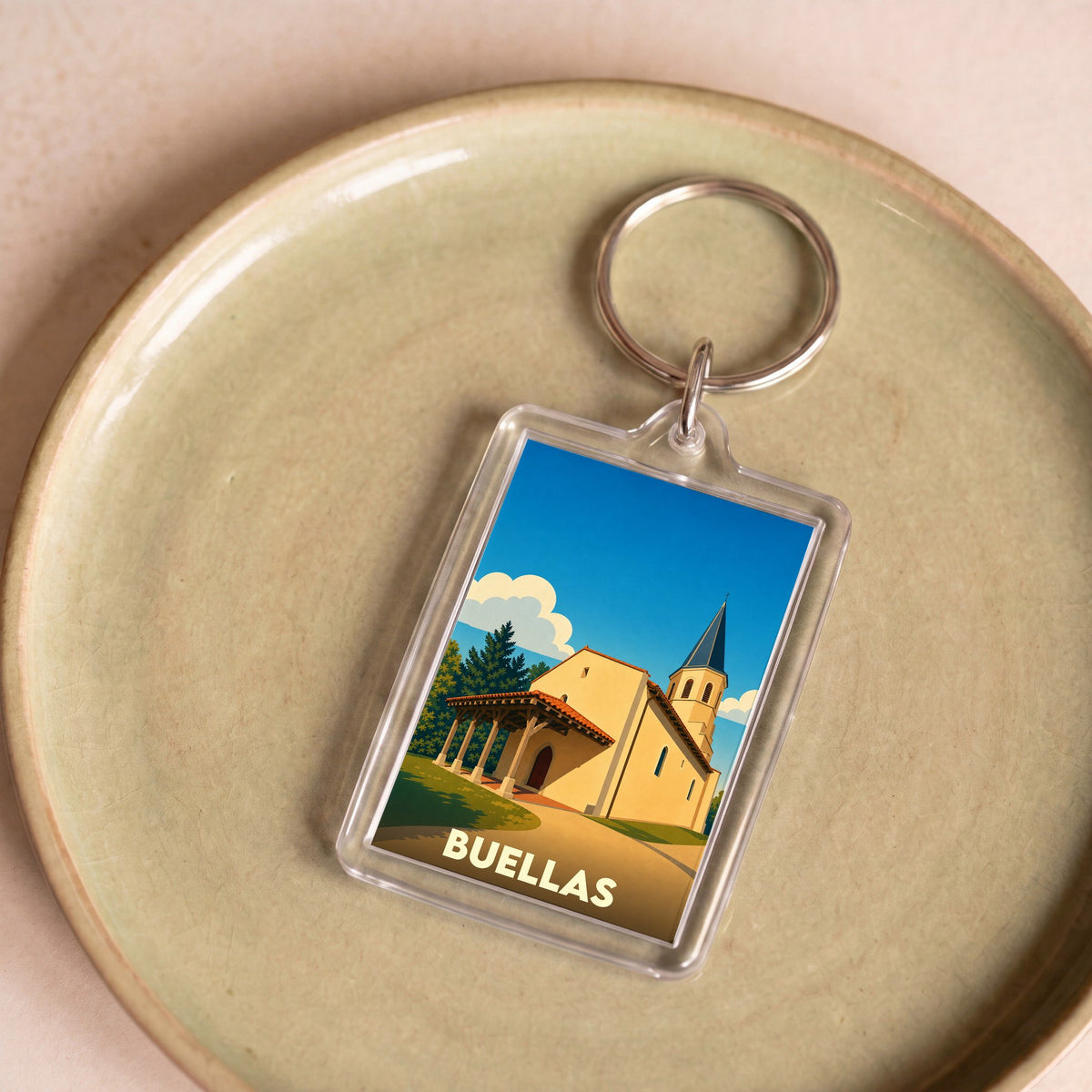 Porte-clés souvenir de la ville de Buellas avec une illustration stylisée d'une église sous un ciel bleu.