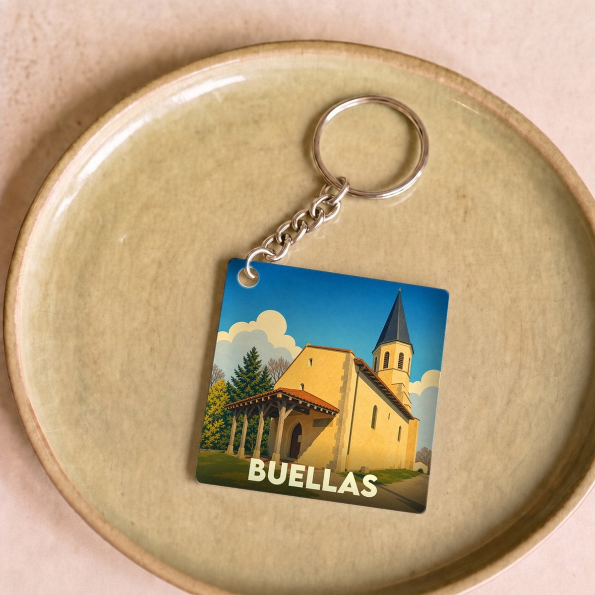 Porte-clés souvenir de la ville de Buellas avec une illustration stylisée d'une église sous un ciel bleu.