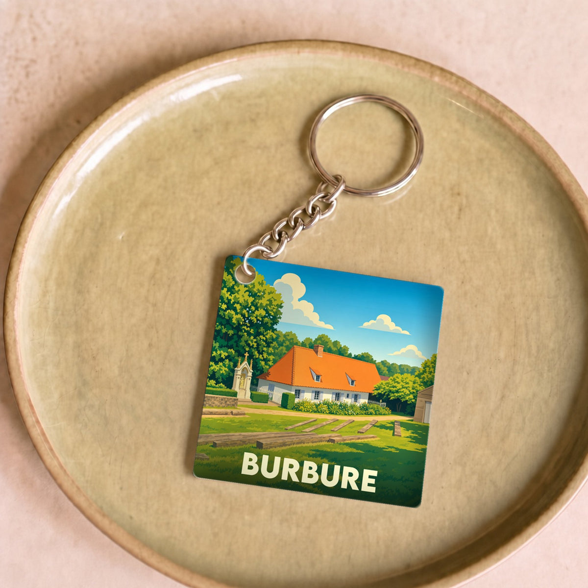 Porte-clés souvenir de la ville de Burbure avec une illustration stylisée d'une maison rurale sous un ciel bleu.