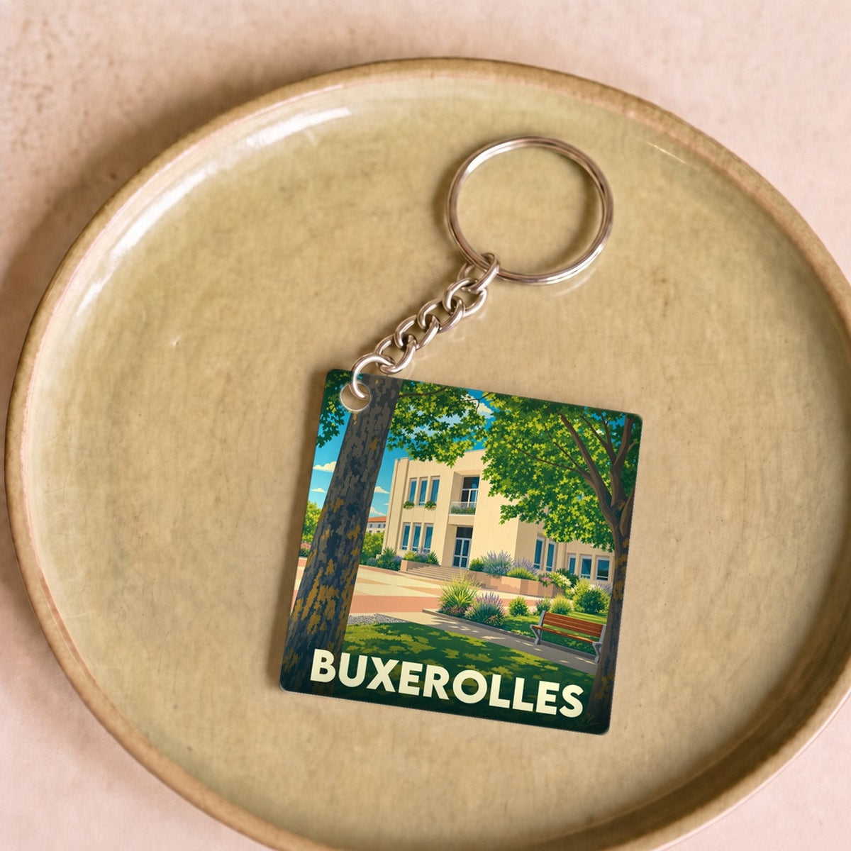 Porte-clés souvenir de la ville de Buxerolles avec une illustration stylisée d'un parc boisé devant un bâtiment.