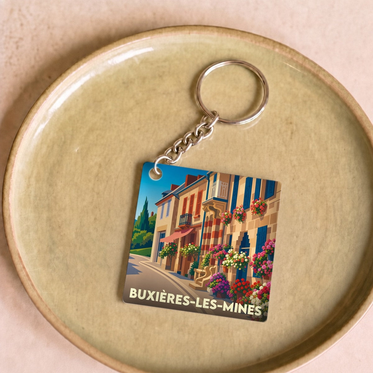 Porte-clés souvenir de la ville de Buxières-les-Mines avec une illustration colorée et stylisée d'une rue fleurie.