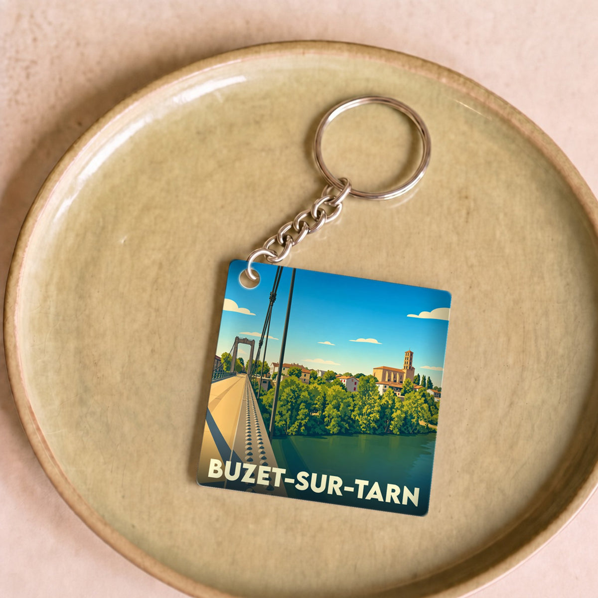 Porte-clés souvenir de la ville de Buzet-sur-Tarn avec une illustration stylisée d'un pont suspendu.