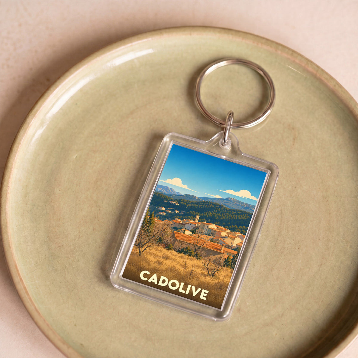 Porte-clés souvenir de la ville de Cadolive avec une illustration stylisée d'un paysage provençal.