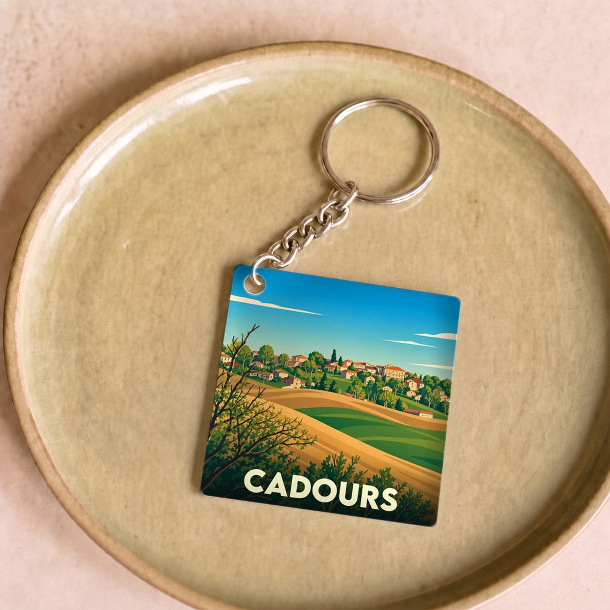 Porte-clés souvenir de la ville de Cadours avec une illustration stylisée de paysages vallonnés.