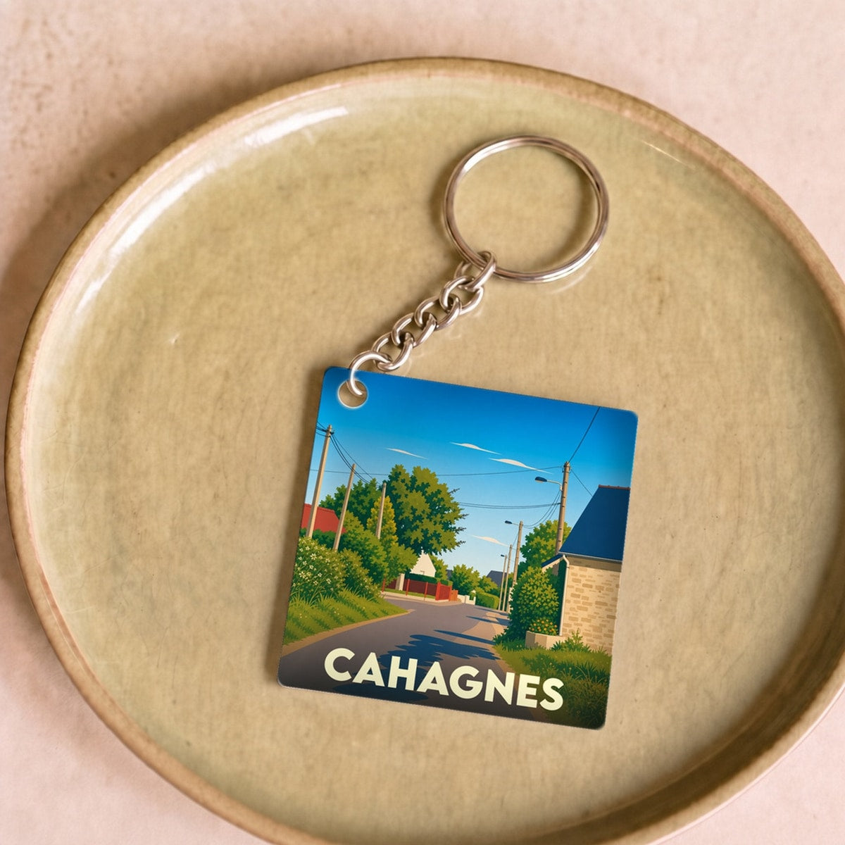 Porte-clés souvenir de la ville de Cahagnes avec une illustration stylisée d'une route de campagne.