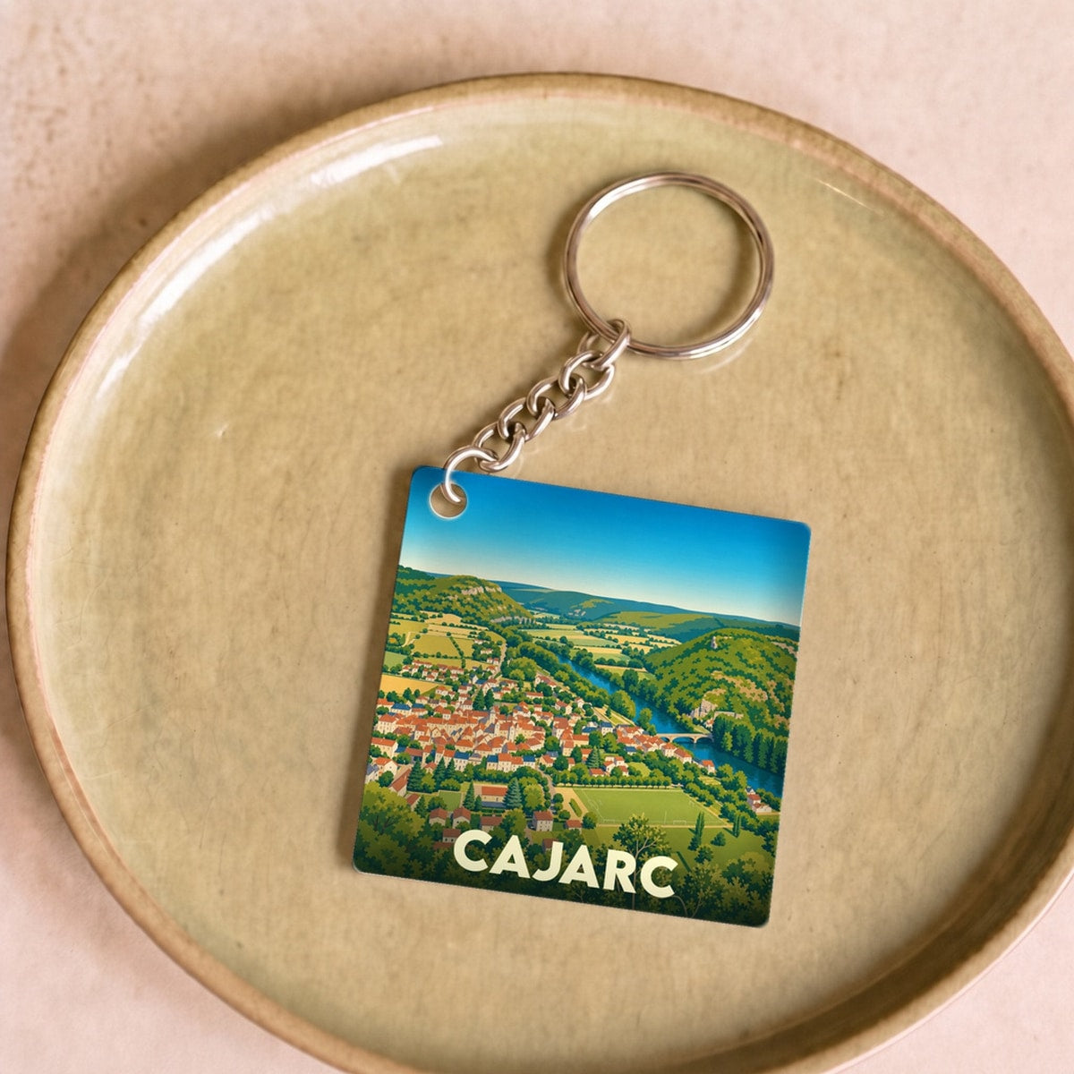 Porte-clés souvenir de la ville de Cajarc avec une illustration stylisée d'un paysage panoramique.