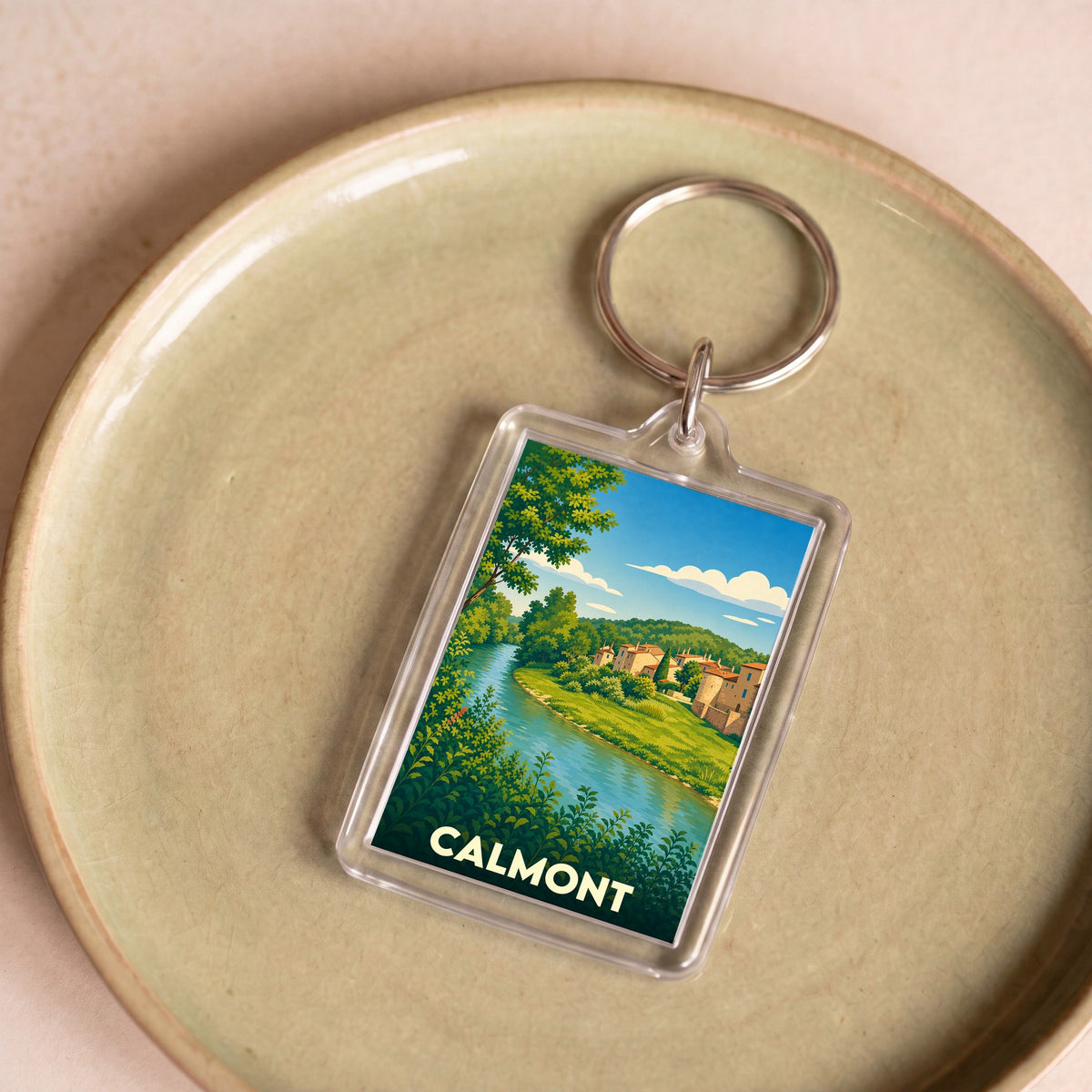 Porte-clés souvenir de la ville de Calmont avec une illustration stylisée d'un paysage de rivière.