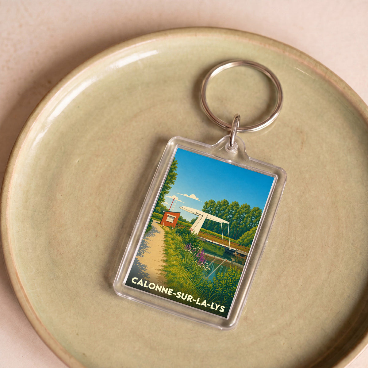 Porte-clés souvenir de la ville de Calonne-sur-la-Lys avec une illustration stylisée d'un pont levant au-dessus de l'eau.