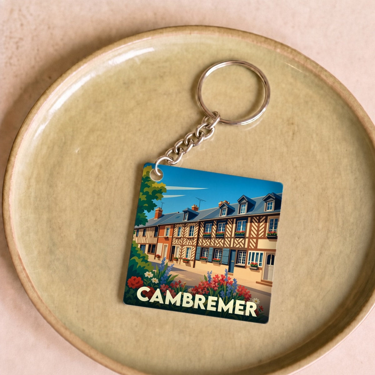 Porte-clés souvenir de la ville de Cambremer avec une illustration stylisée de maisons normandes fleuries.