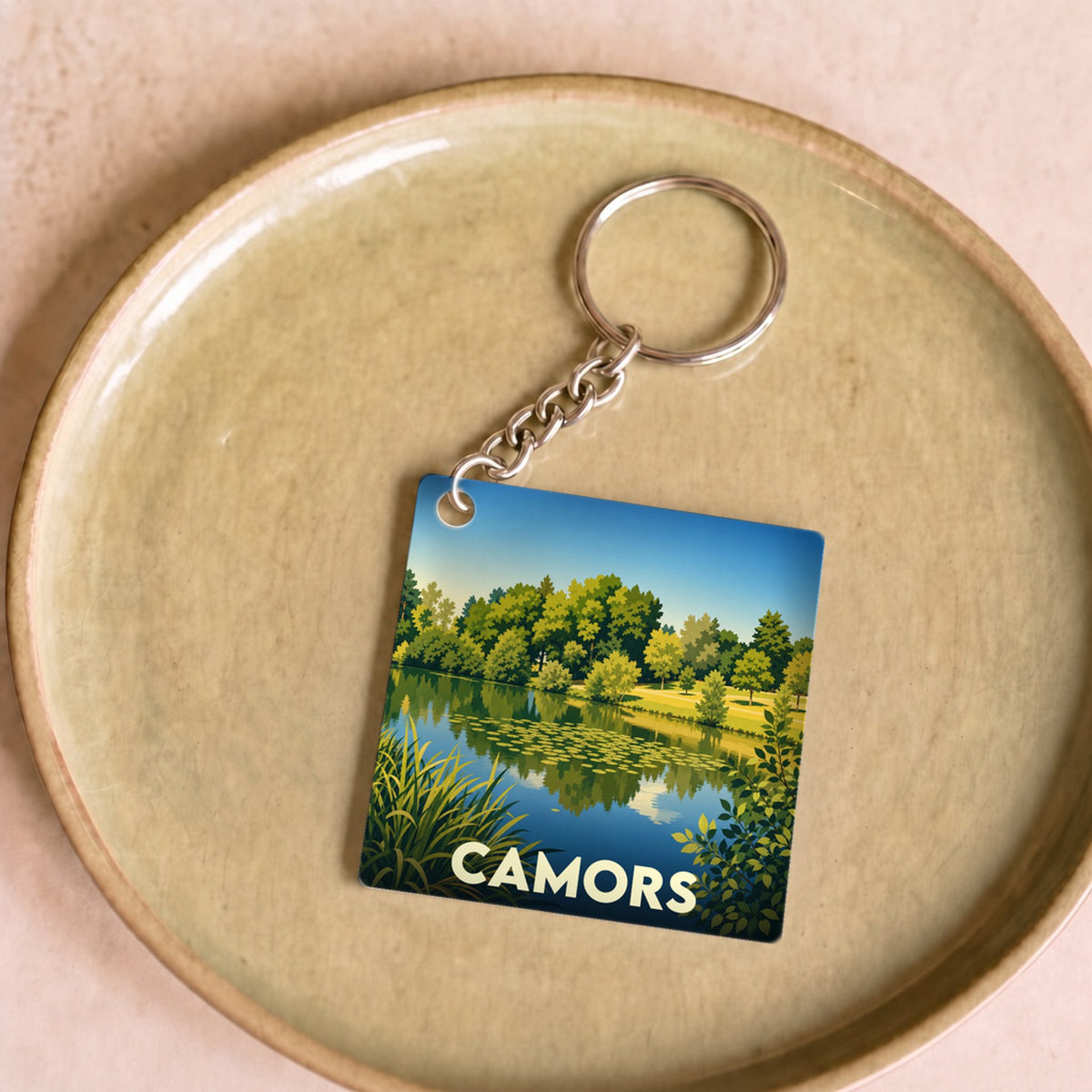Porte-clés souvenir de la ville de Camors avec une illustration stylisée d'un étang boisé.