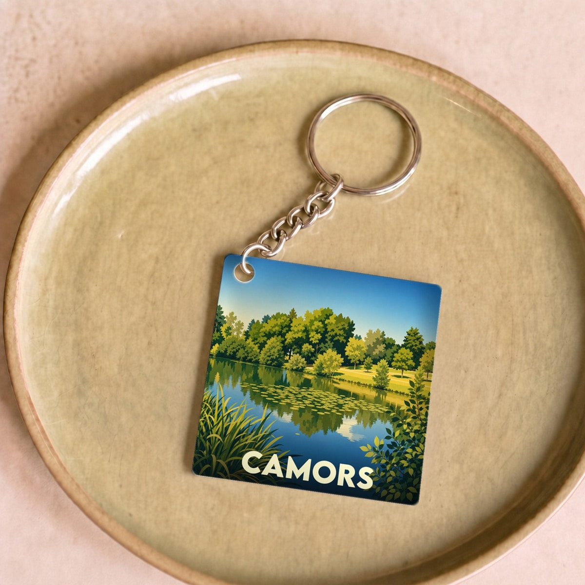 Porte-clés souvenir de la ville de Camors avec une illustration stylisée d'un étang boisé.