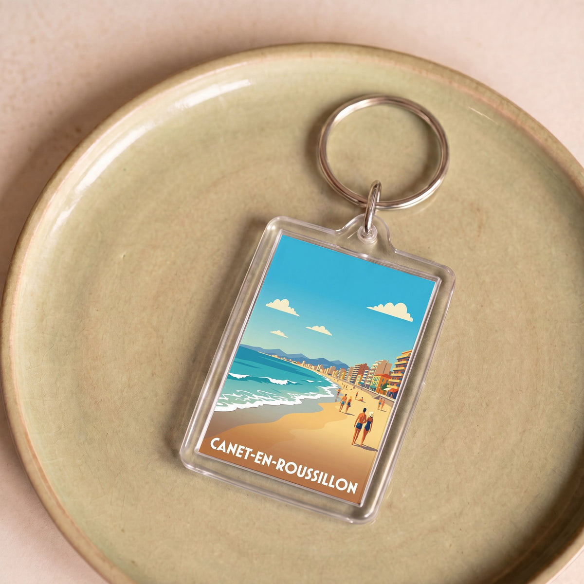 Porte-clés souvenir de la ville de Canet-en-Roussillon avec une illustration de plage stylisée.