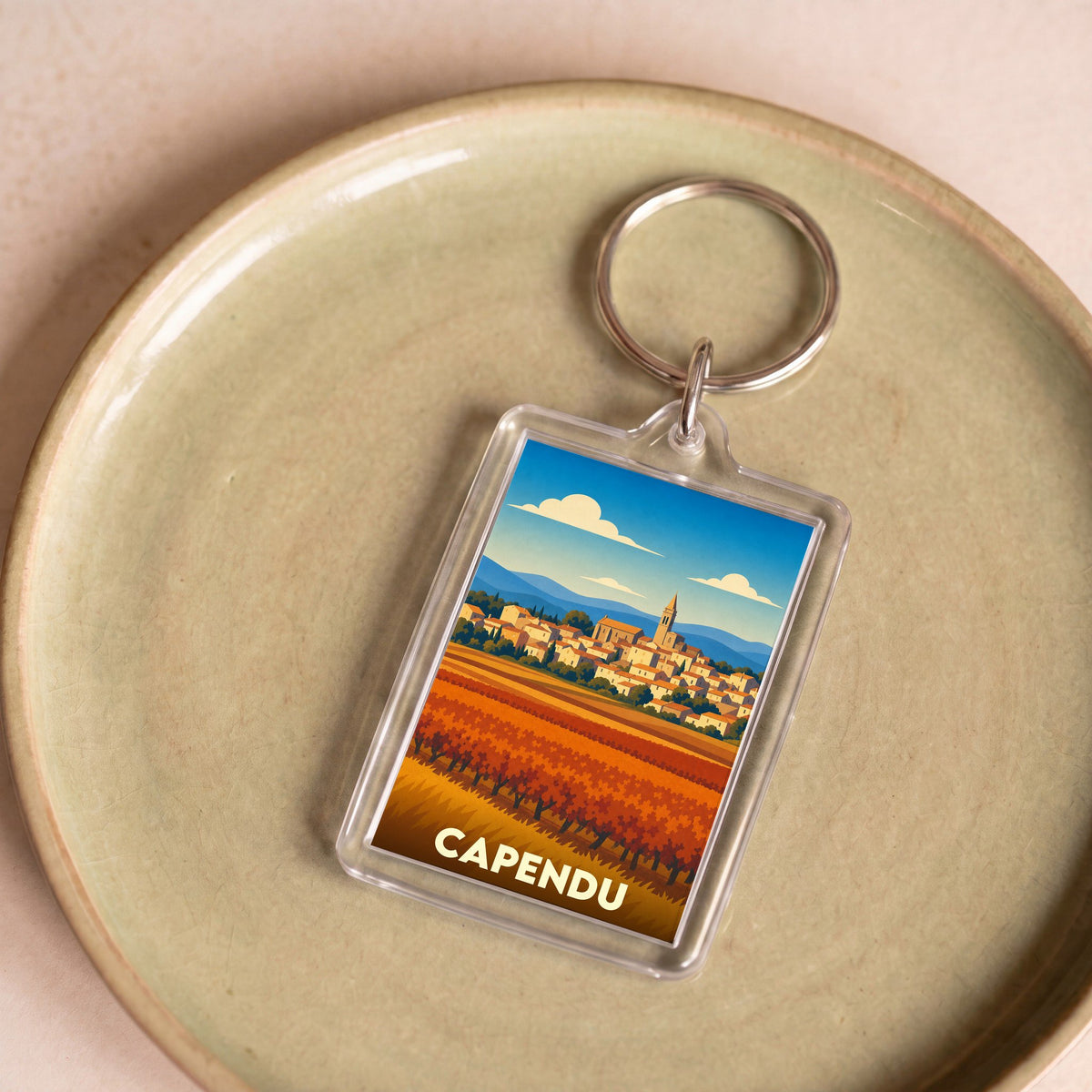 Porte-clés souvenir de la ville de Capendu avec une illustration stylisée d'un paysage de vignes et de village.