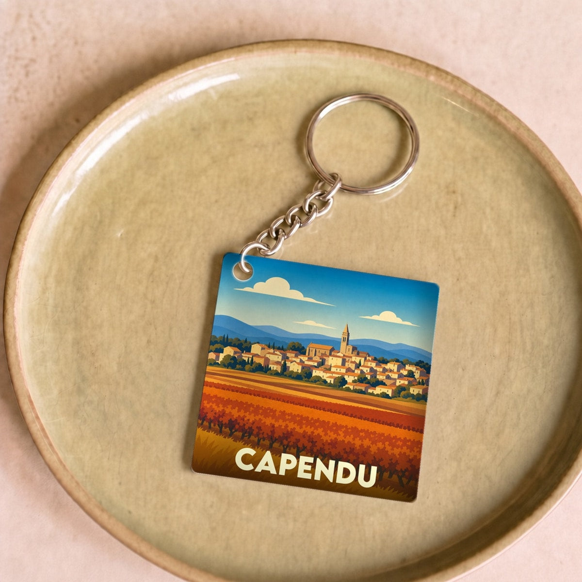 Porte-clés souvenir de la ville de Capendu avec une illustration stylisée d'un paysage de vignes et de village.