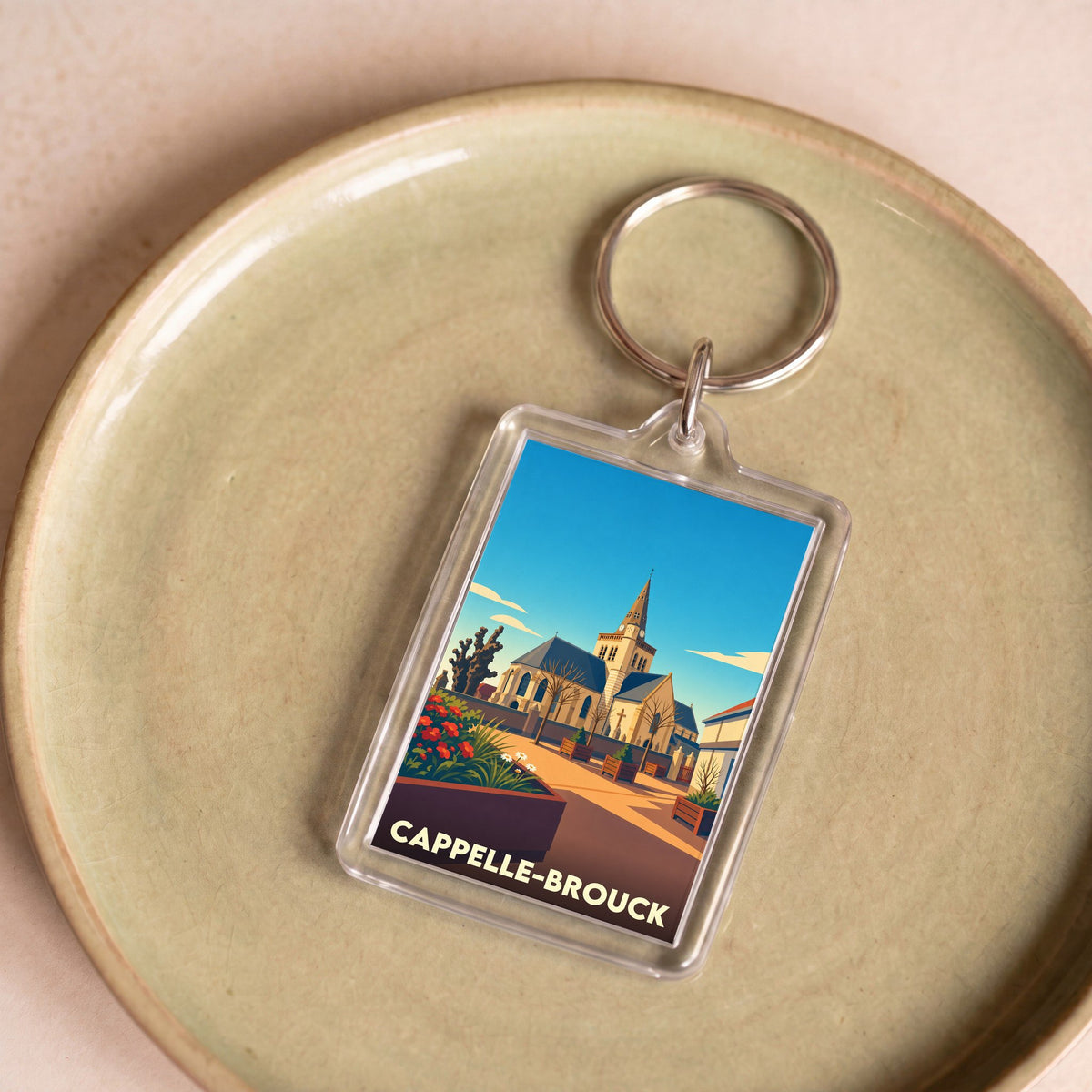 Porte-clés souvenir de la ville de Cappelle-Brouck avec une illustration stylisée de son église.