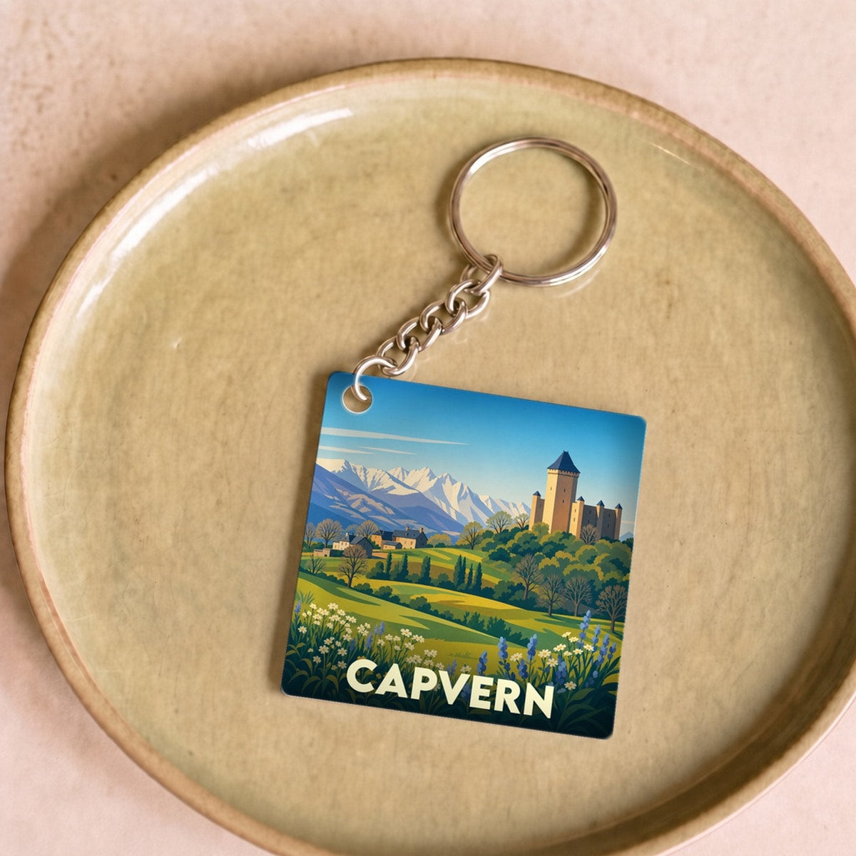 Porte-clés souvenir de la ville de Capvern avec une illustration stylisée des montagnes et d'un château.
