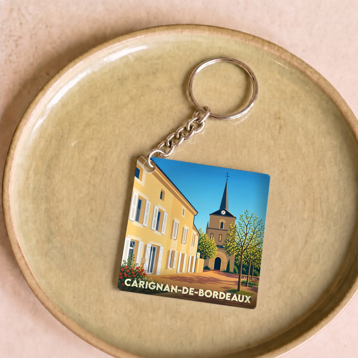 Porte-clés souvenir de Carignan-de-Bordeaux illustrant le centre du village dans un style graphique épuré.