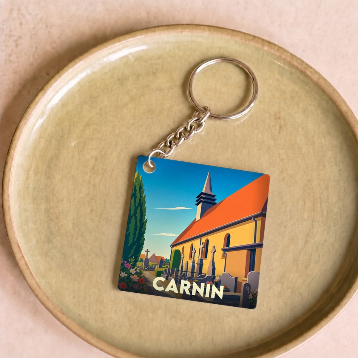 Porte-clés souvenir de la ville de Carnin avec une illustration stylisée de son église et de son cimetière.