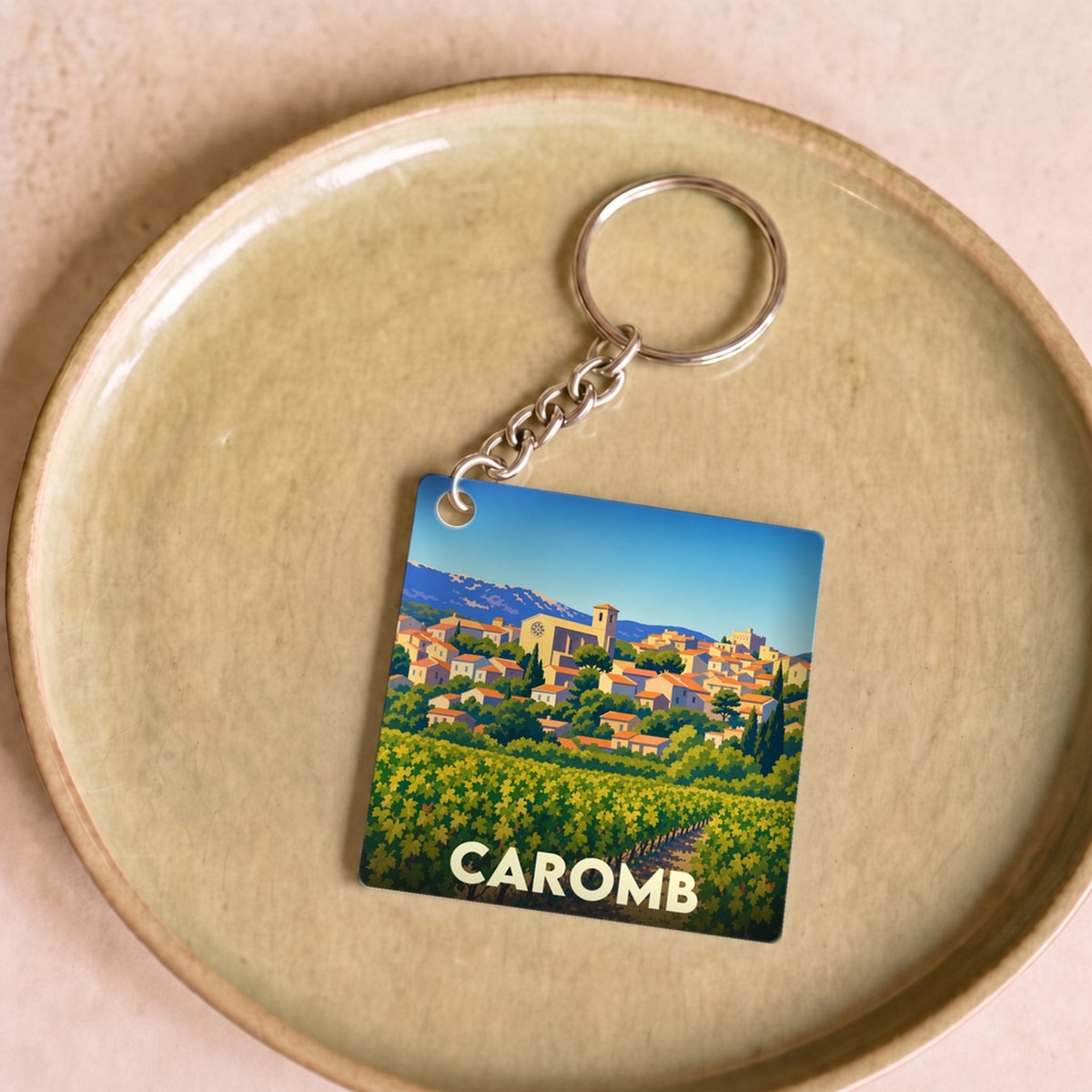 Porte-clés souvenir de la ville de Caromb avec une illustration stylisée d'un paysage provençal.