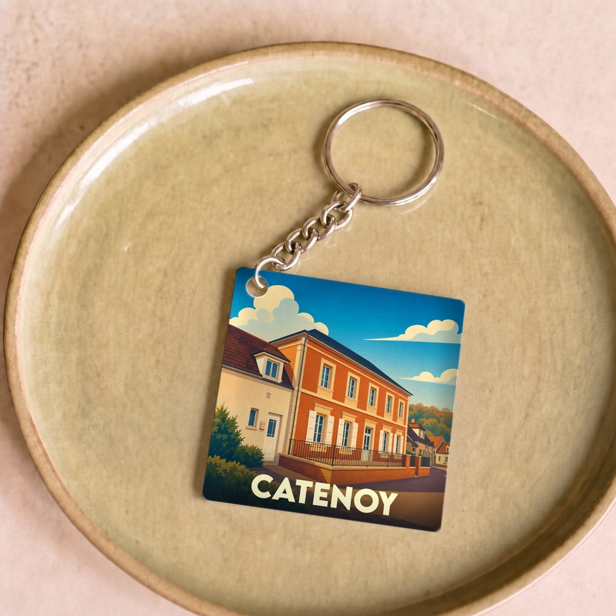 Porte-clés souvenir de la ville de Catenoy avec une illustration stylisée d'un bâtiment sous un ciel bleu.