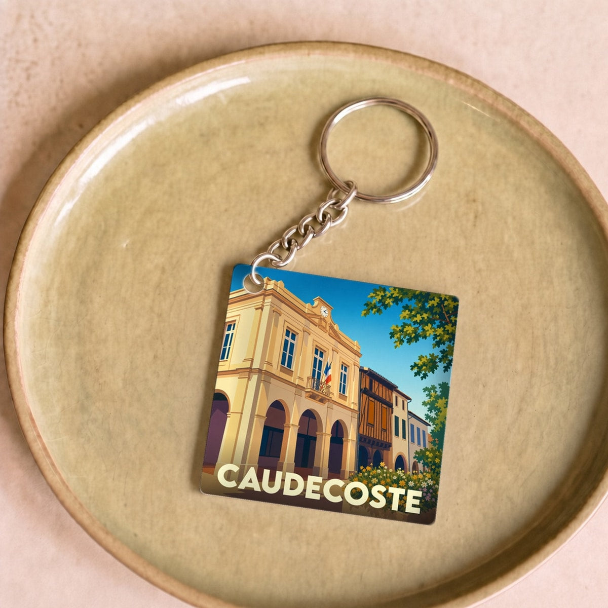 Porte-clés souvenir de la ville de Caudecoste avec une illustration stylisée.
