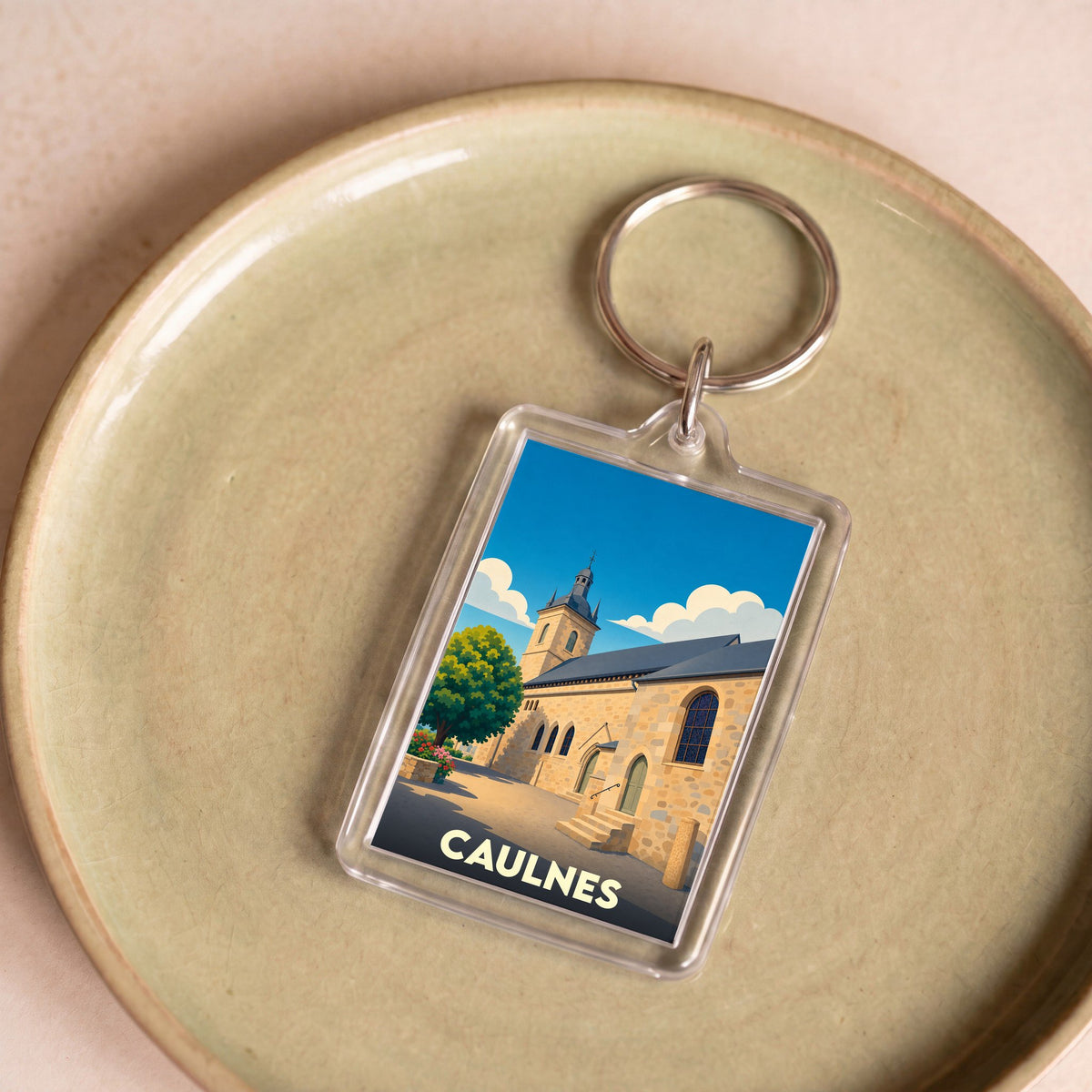 Porte-clés souvenir de la ville de Caulnes avec une illustration stylisée d'une église sous un ciel bleu.