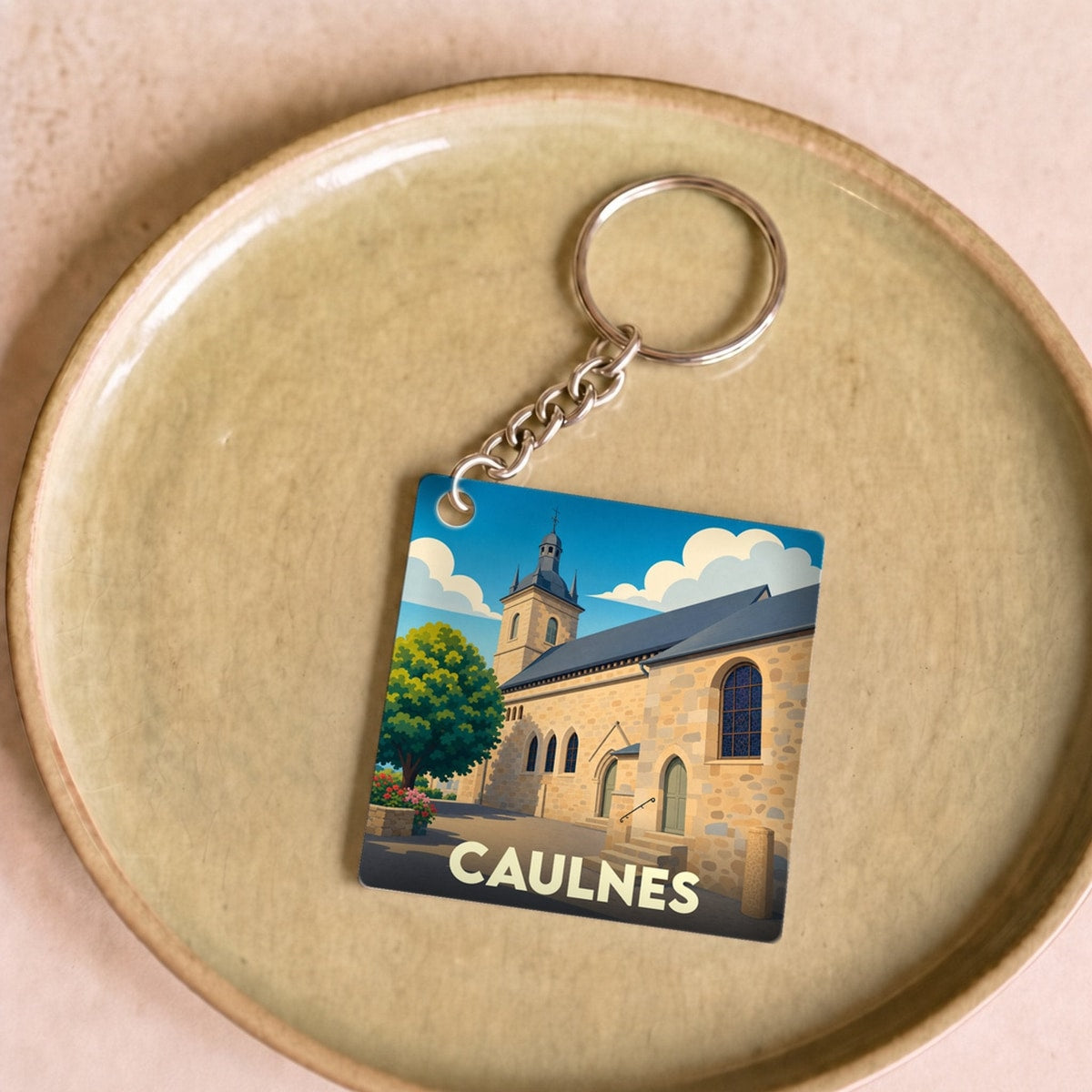 Porte-clés souvenir de la ville de Caulnes avec une illustration stylisée d'une église sous un ciel bleu.