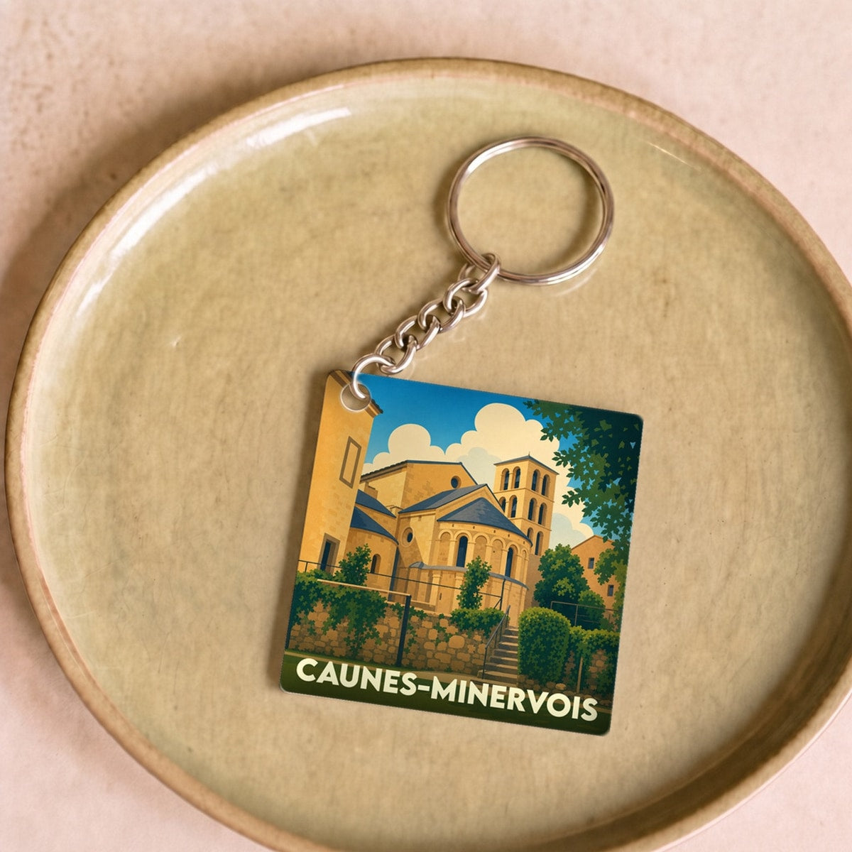 Porte-clés souvenir de la ville de Caunes-Minervois avec une illustration stylisée de son abbaye.