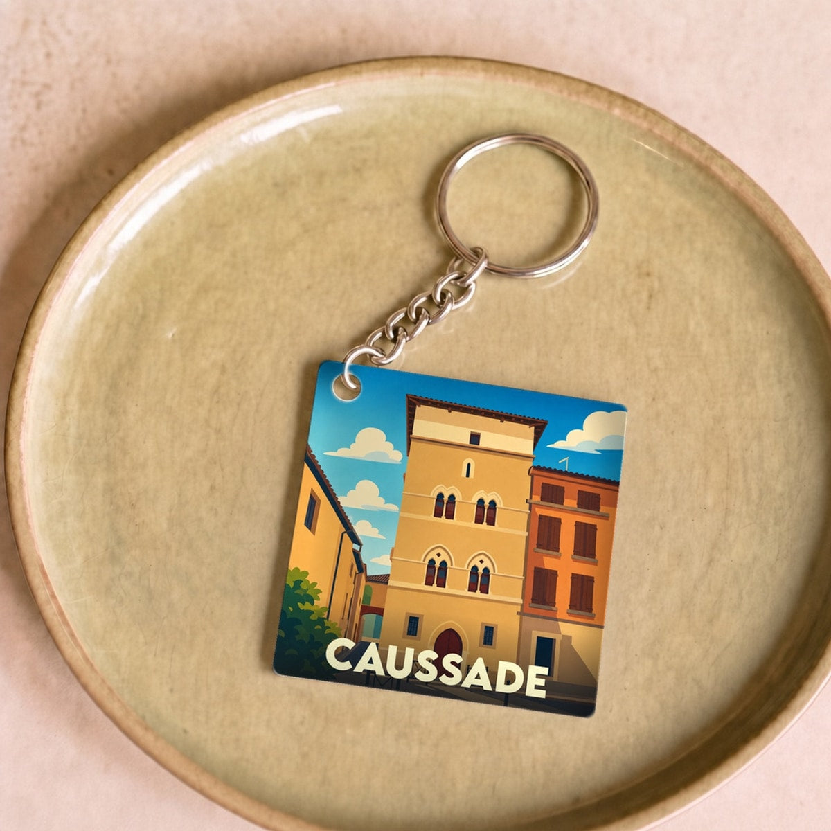 Porte-clés souvenir de la ville de Caussade avec une illustration stylisée de son architecture historique.