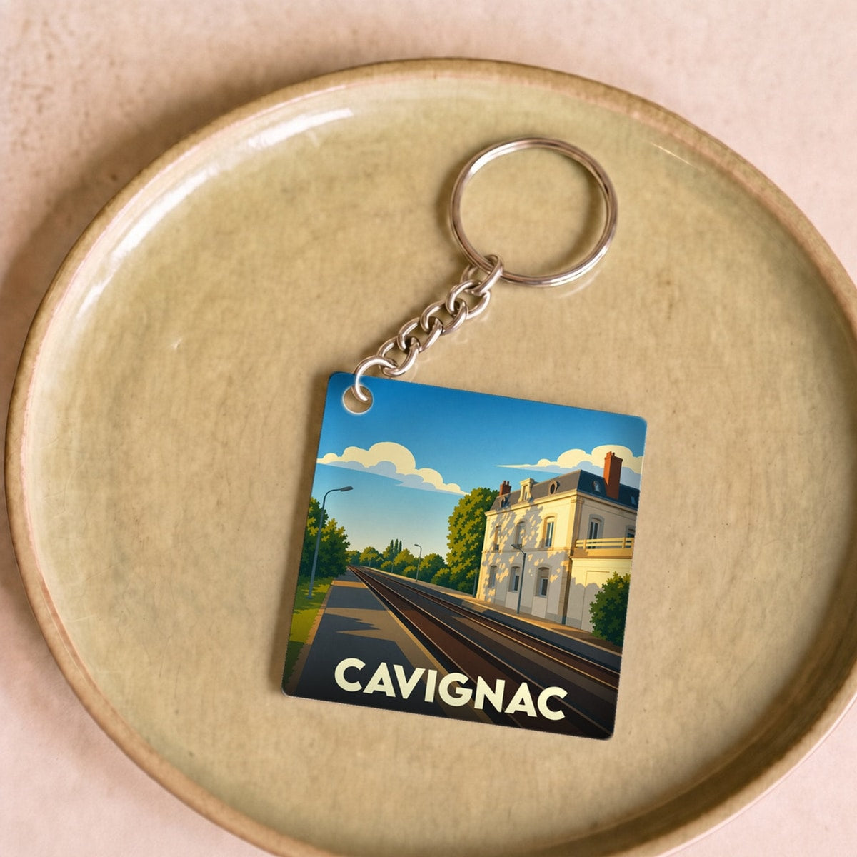 Porte-clés souvenir de la ville de Cavignac avec une illustration stylisée d'une gare sous un ciel bleu.