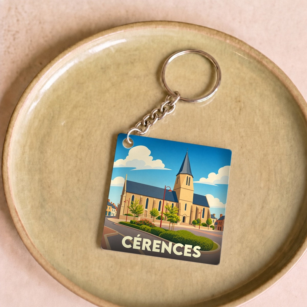 Porte-clés souvenir de la ville de Cérences avec une illustration stylisée de son église sous un ciel bleu.