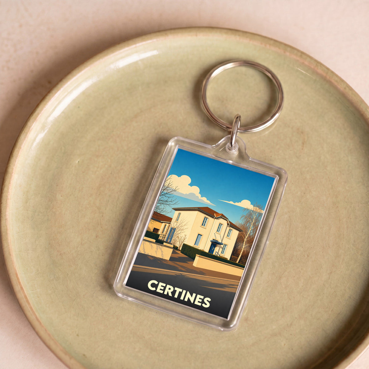 Porte-clés souvenir de la ville de Certines avec une illustration stylisée d'une maison sous un ciel bleu.