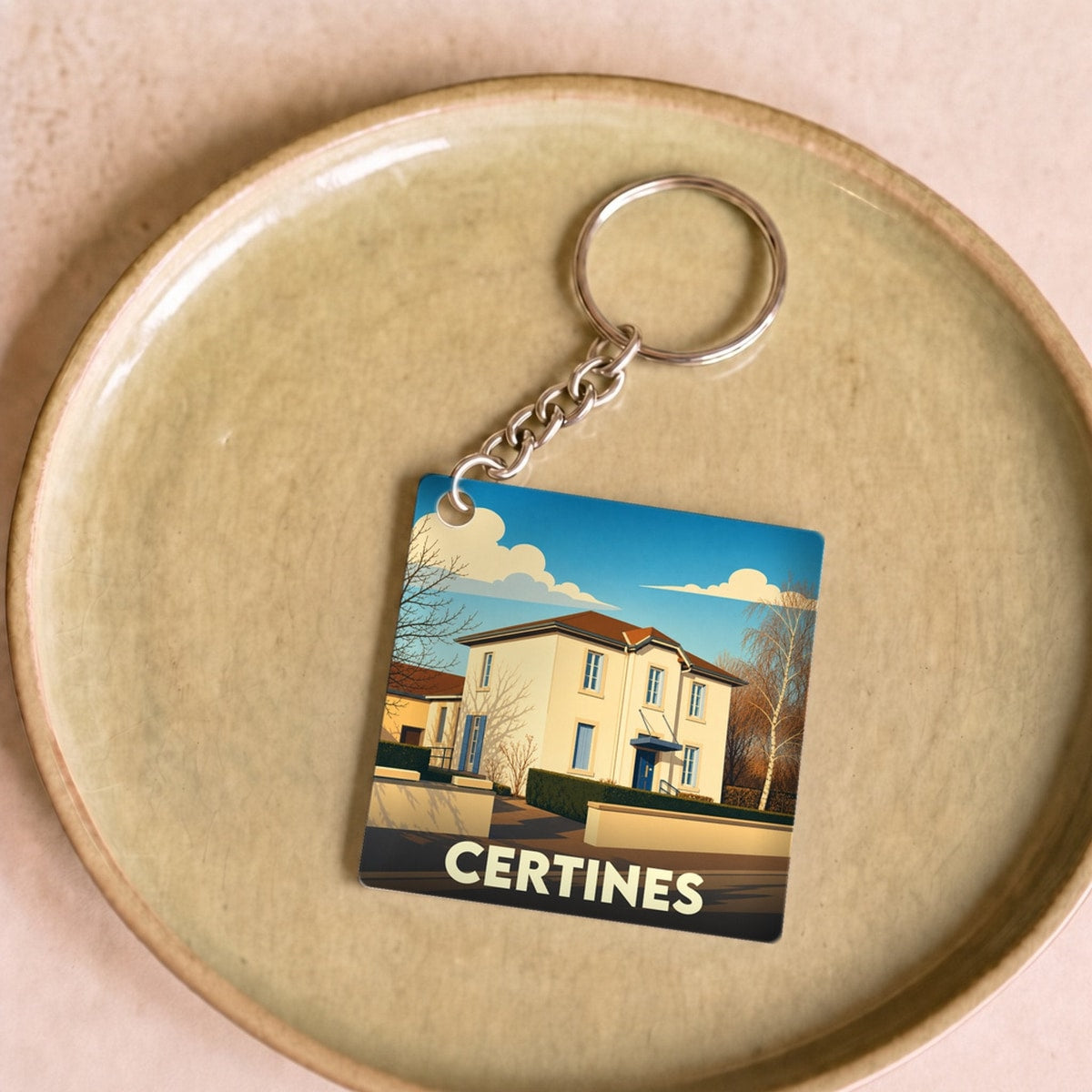 Porte-clés souvenir de la ville de Certines avec une illustration stylisée d'une maison sous un ciel bleu.