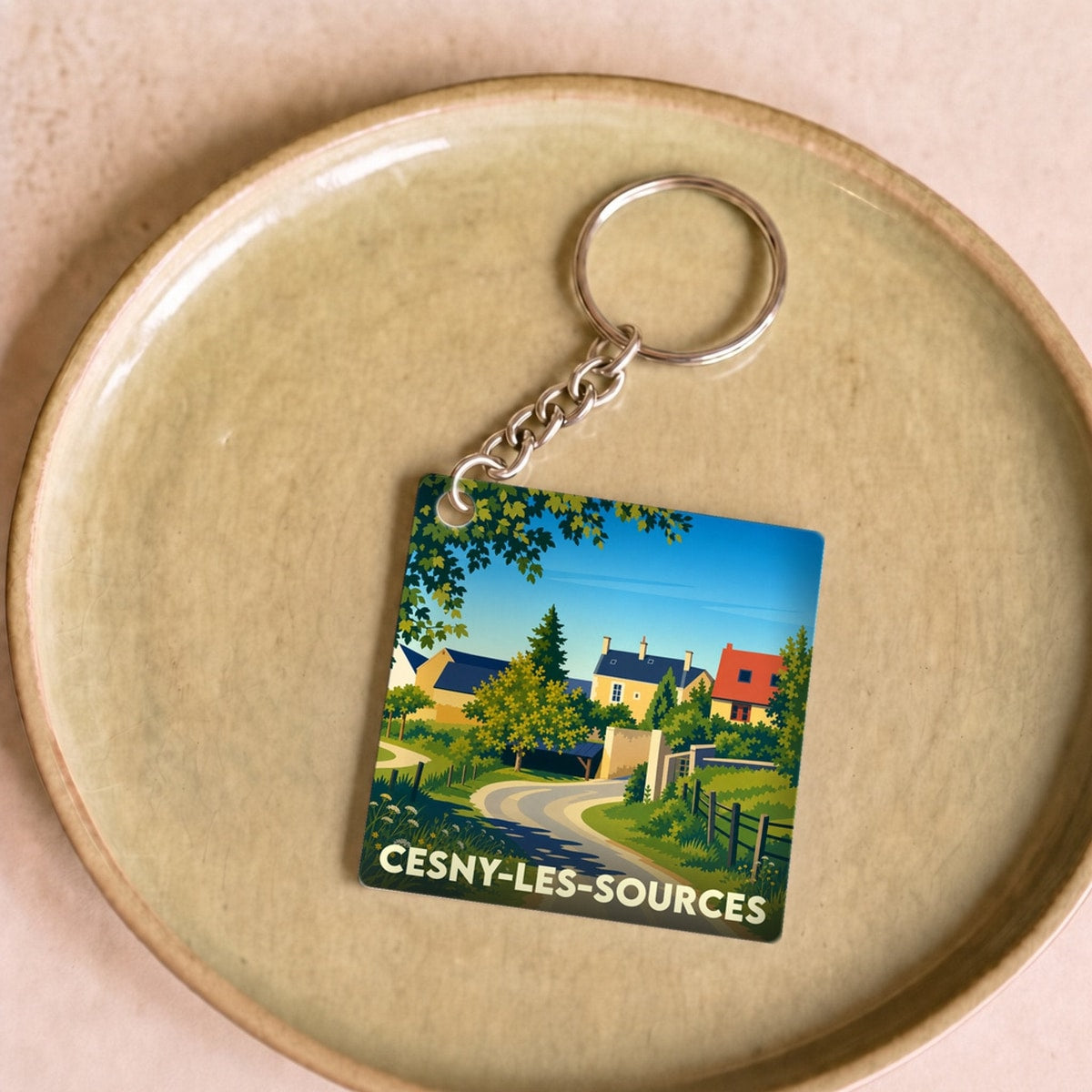 Porte-clés souvenir de la ville de Cesny-les-Sources avec une illustration stylisée d'un paysage de village.